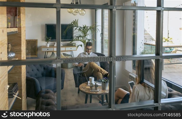Young businessman sitting in waiting room seen through a glass window
