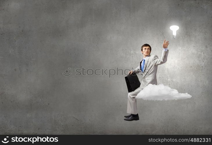 Young businessman sitting on cloud and thinking something over. Waiting for inspiration