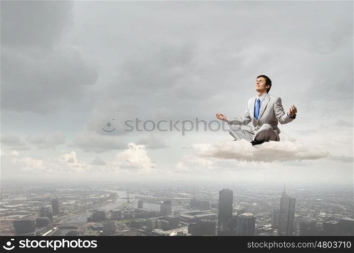 Young businessman sitting on cloud high in sky and meditating. Waiting for inspiration