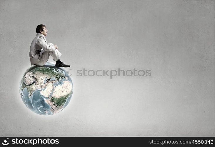 Young businessman sitting on Earth planet. Elements of this image are furnished by NASA. On top of world
