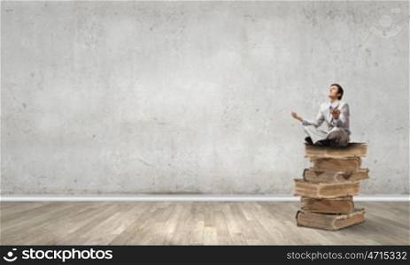 Young businessman sitting on pile of old books and meditating. Knowledge advantage