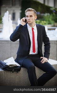 Young businessman sitting on platform while using cell phone