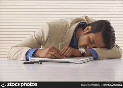 Young businessman sleeping on laptop at desk in office