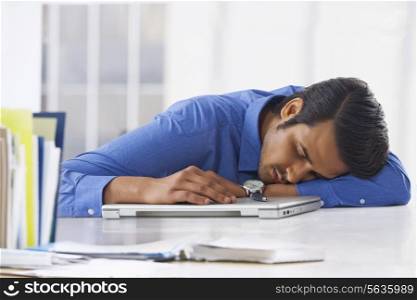 Young businessman sleeping on laptop at office desk