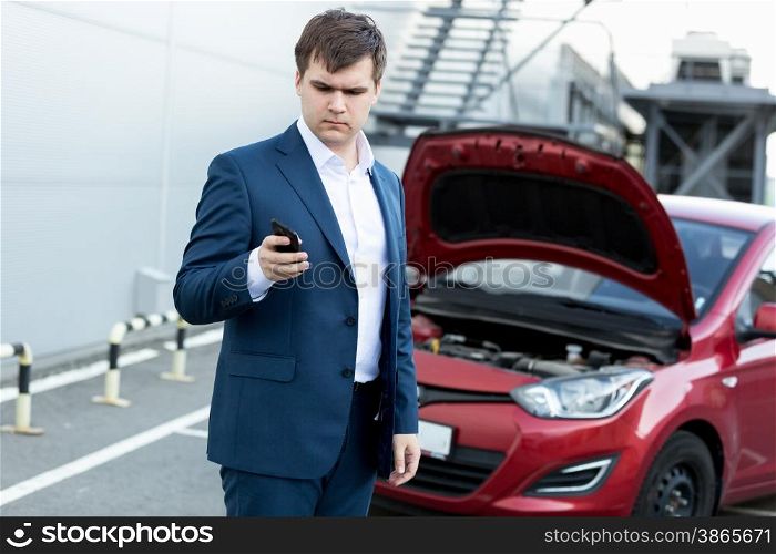 Young businessman standing at broken car and using telephone
