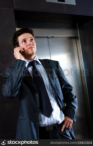 Young businessman standing at office lobby waiting for elevator and calling on mobile phone.