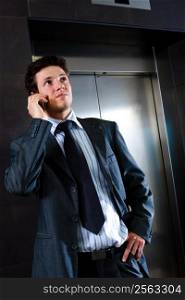 Young businessman standing at office lobby waiting for elevator and calling on mobile phone.