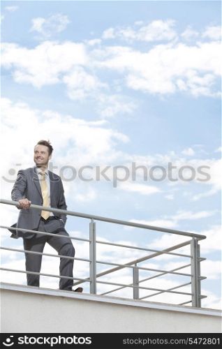 Young businessman standing at terrace railings against sky