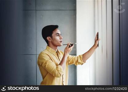 Young Businessman Standing by the Window in Office. Using Voice Control via Smartphone
