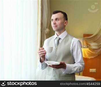 young businessman standing near window with a cup in his hands