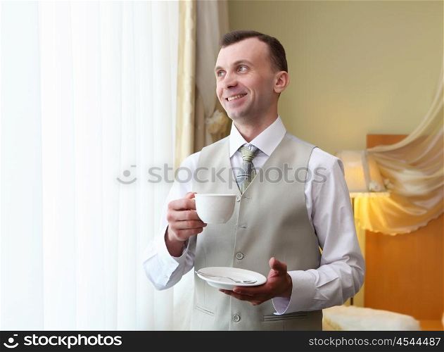 young businessman standing near window with a cup in his hands