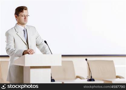 Young businessman standing on stage and speaking to microphone . Speaker at stage