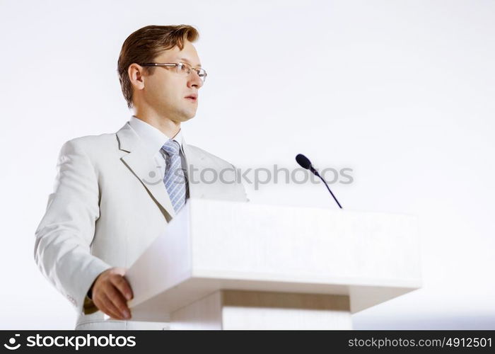 Young businessman standing on stage and speaking to microphone . Speaker at stage