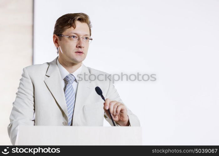 Young businessman standing on stage and speaking to microphone . Speaker at stage