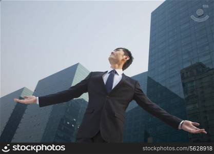 Young businessman standing outside with arms outstretched