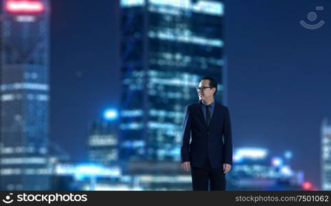 Young businessman standing with out of focus city skyscraper background . Night scene.