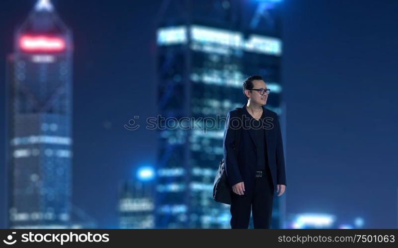 Young businessman standing with out of focus city skyscraper background . Night scene.