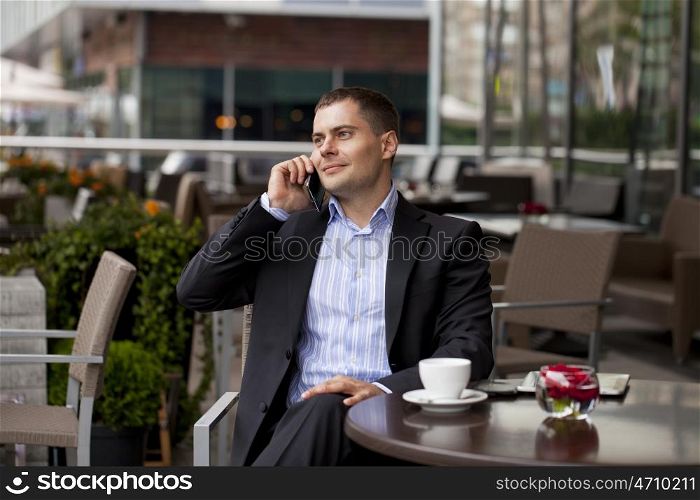 Young businessman talking on a cell phone while sitting in a summer cafe
