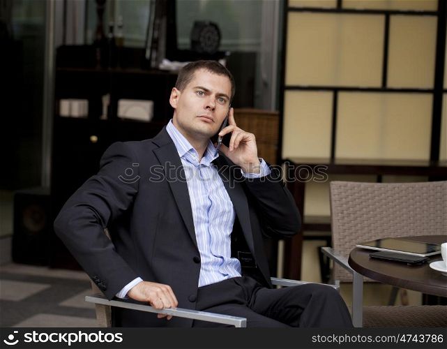 Young businessman talking on a cell phone while sitting in a summer cafe