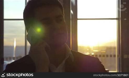 Young businessman talking on cell phone at the airport by the window with sunset view