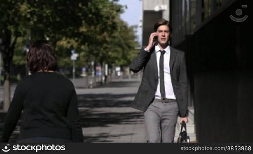 Young businessman talking on mobile phone and walking in the street. Slow motion