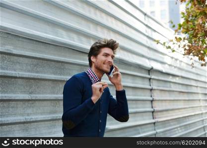 Young businessman talking smartphone phone on the street metal fence