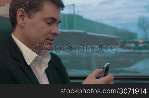 Young businessman texting on smartphone or browsing in internet while traveling by train. Communication in business trip
