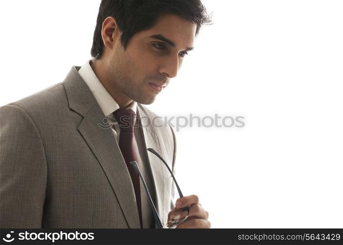 Young businessman thinking while holding glasses over white background