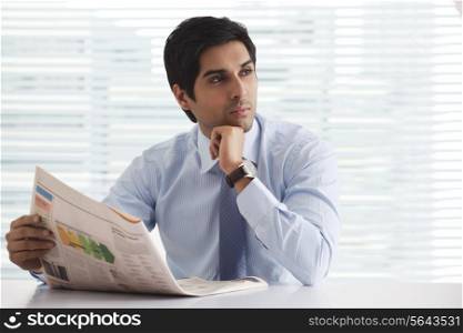 Young businessman thinking with newspaper at office