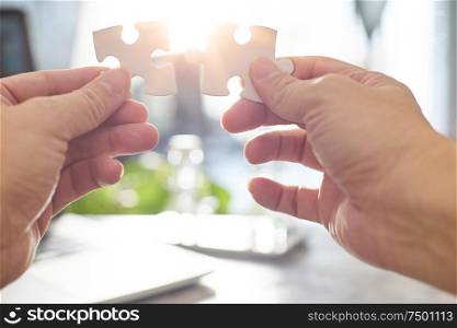 Young businessman trying to connect couple puzzle piece with sun flare and blur background,symbol of association and connection. business strategy.