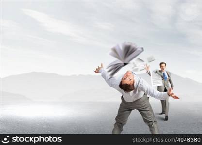 Young businessman trying to evade from thrown book. Two business people fighting with each other