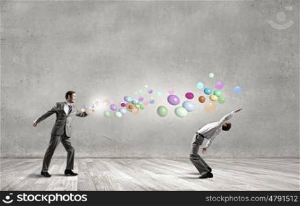 Young businessman trying to evade from thrown colorful balloons