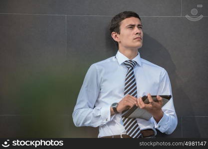 Young businessman using a tablet while leaning on a wall of modern building in the city