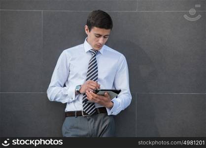 Young businessman using a tablet while leaning on a wall of modern building in the city