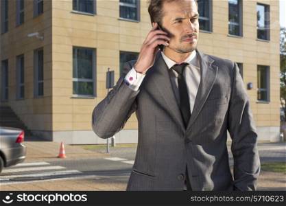 Young businessman using cell phone against office building