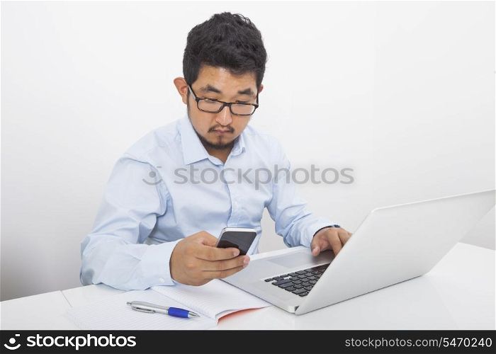Young businessman using cell phone while working at desk in office