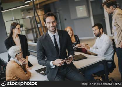 Young businessman using digital tablet in office in front of his team