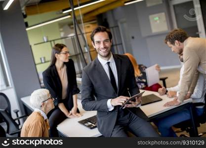 Young businessman using digital tablet in office in front of his team