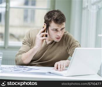 Young businessman using laptop while on call