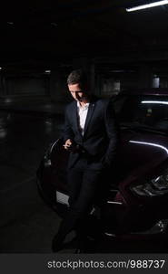 young businessman using smart phone while standing near his car. A young man in a suit stands near the car and holds a telephone