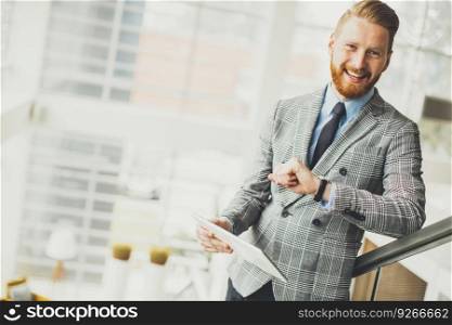 Young businessman using tablet and looking at his watch