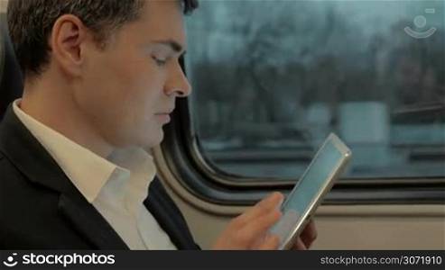 Young businessman using tablet computer during train ride. Easy work and entertainment with wireless device