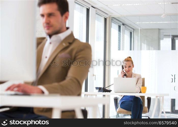 Young businessman using telephone with male colleague in foreground at office