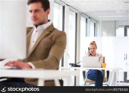Young businessman using telephone with male colleague in foreground at office