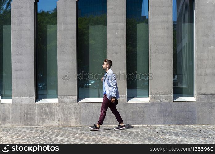 Young businessman walking next to office buildings while holding a shoulder bag outdoors