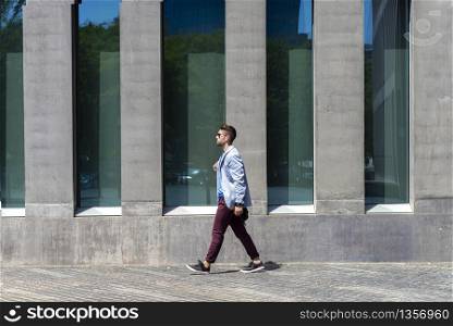 Young businessman walking next to office buildings while holding a shoulder bag outdoors
