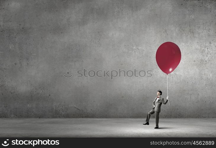 Young businessman walking with colorful balloon on rope