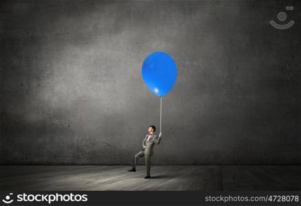 Young businessman walking with colorful balloon on rope