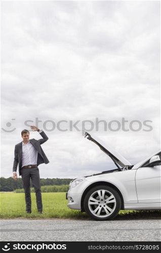 Young businessman waving for help by broken down car at countryside