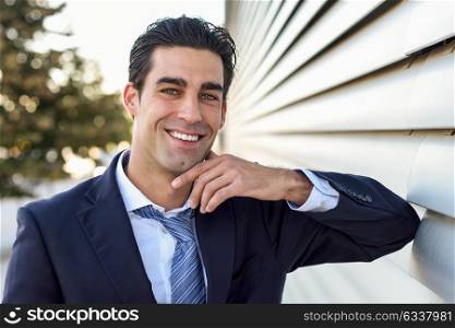 Young businessman wearing blue suit and tie in urban background. Man with formal clothes in the street. Blue eyes guy with toothy smile.